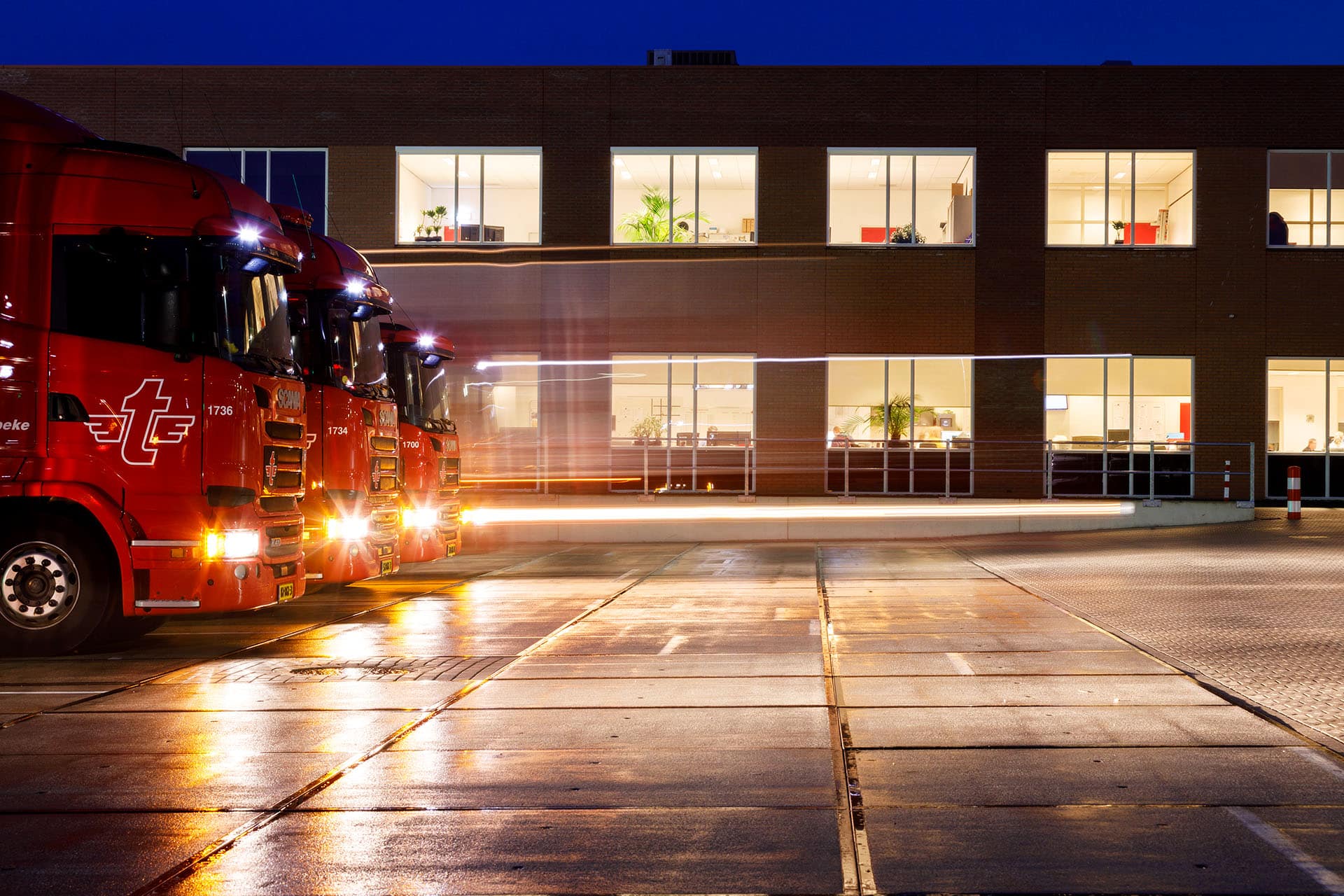 drie vrachtwagens met verlichting aan in het donker bij kantoor