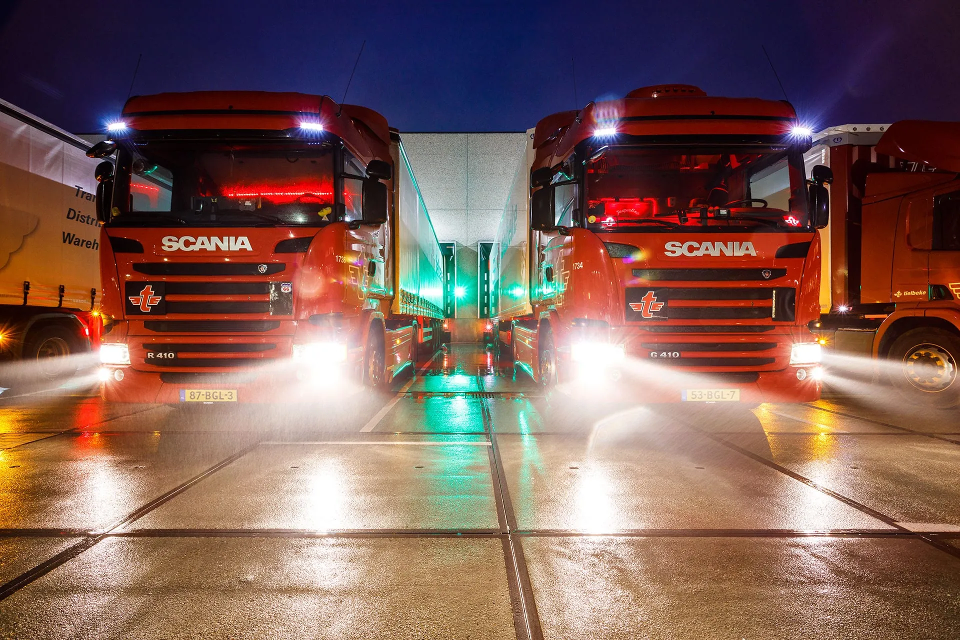 twee vrachtwagens met verlichting aan in het donker aan laaddock