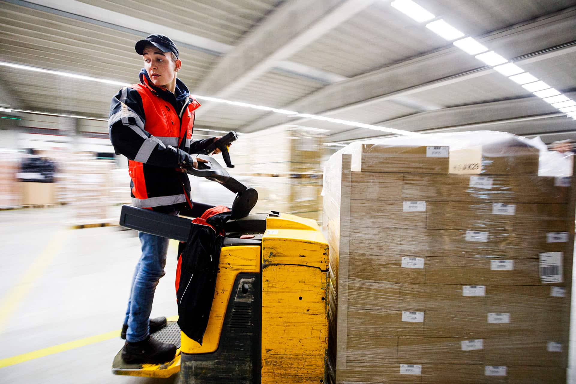 Loodsmedewerker rijdend door loods op elektrische pallet truck