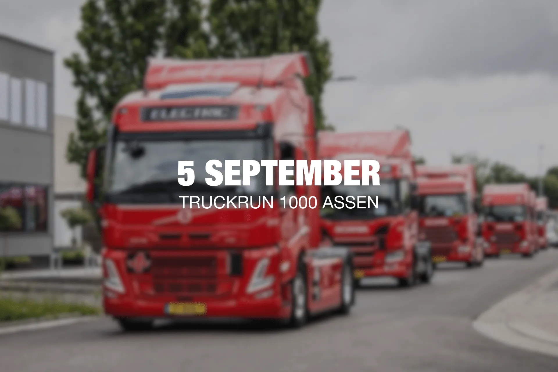 Convoy of red trucks driving down a street for the 5 September TruckRun 1000 Assen event.